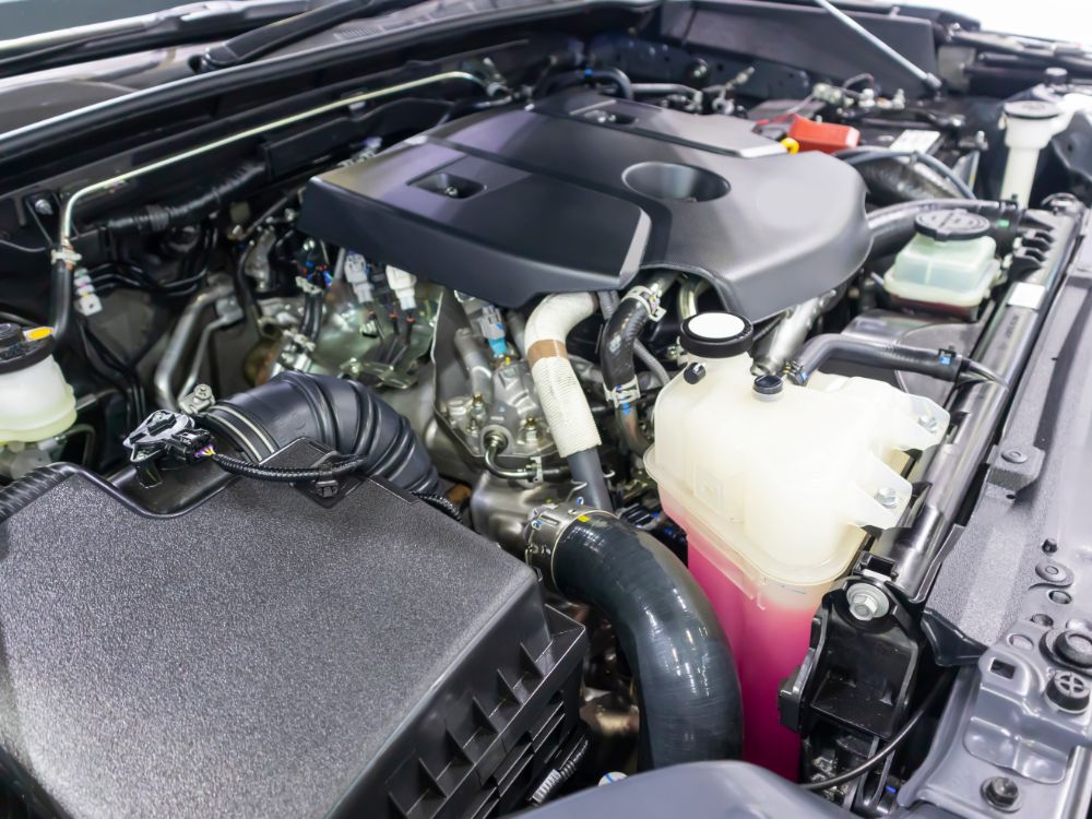 Compartimento do motor de veículo moderno com componentes mecânicos, mangueiras e reservatório de fluido, representando estrutura e engenharia automotiva.